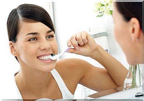 Prevent bad breath: A woman looks in the mirror while brushing her teeth.